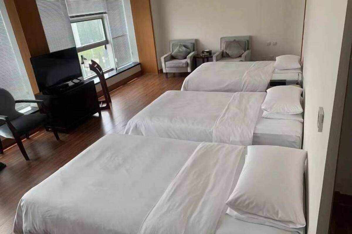 A hotel room with three beds, a TV, a desk, and a chair.