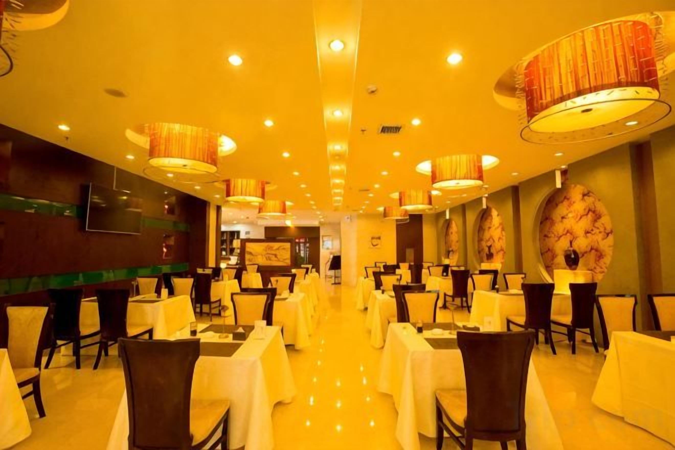 A hotel dining area with round tables, chairs, and hanging lamps.