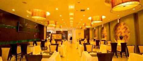 A hotel dining area with round tables, chairs, and hanging lamps.
