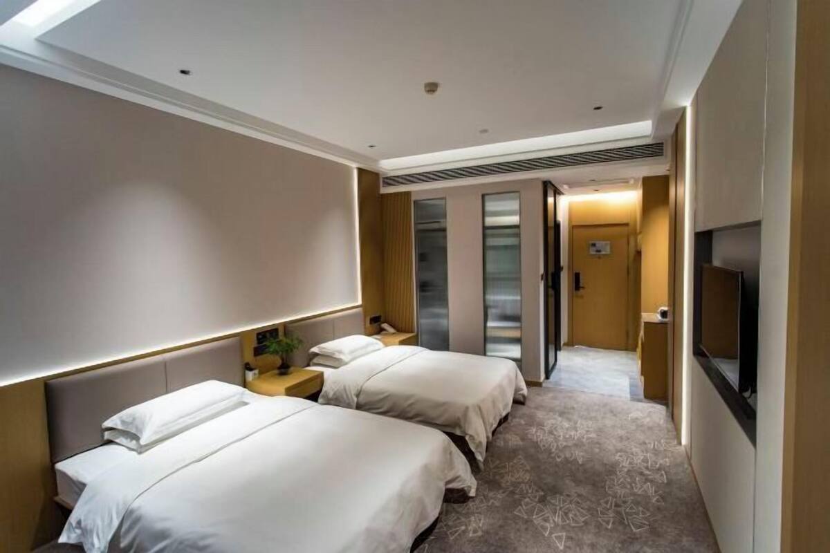 A hotel room with two beds, a TV, a desk, and a bathroom with a mirror and sink.