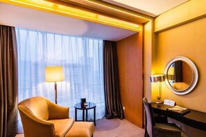 A hotel room with a sofa, a small table, a desk, a chair, a round mirror, and a large window with curtains. - Phoenix International Hotel (Jincheng)