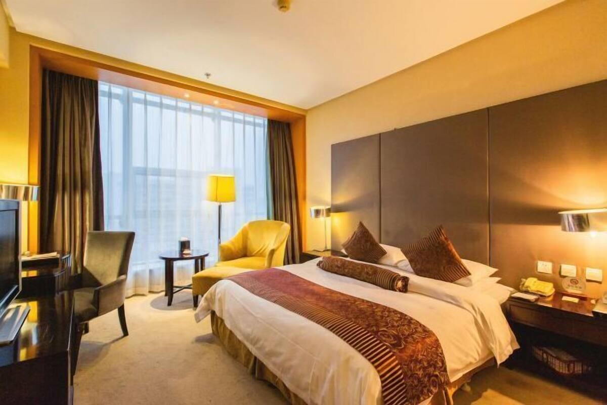 A hotel room with a large bed, a desk, a chair, a TV, and a lamp.