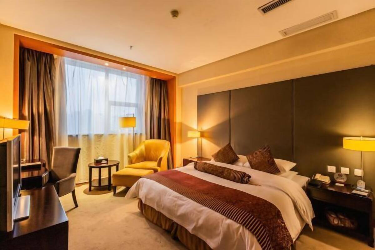 A hotel room with a bed, a desk, a chair, a TV, and a nightstand with a lamp.