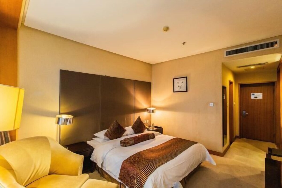 A hotel room with a bed, bedside lamps, a chair, and a door.