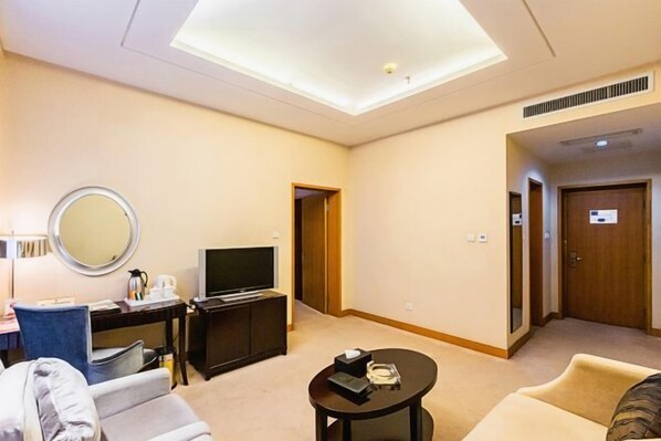 A hotel room with a flat-screen TV, a round mirror, a small table with a remote, a sofa, and a door leading to another room. - Phoenix International Hotel (Jincheng)