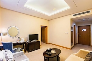 Habitación de hotel con una televisión de pantalla plana, un espejo redondo, una pequeña mesa con un control remoto, un sofá y una puerta que da a otra habitación.