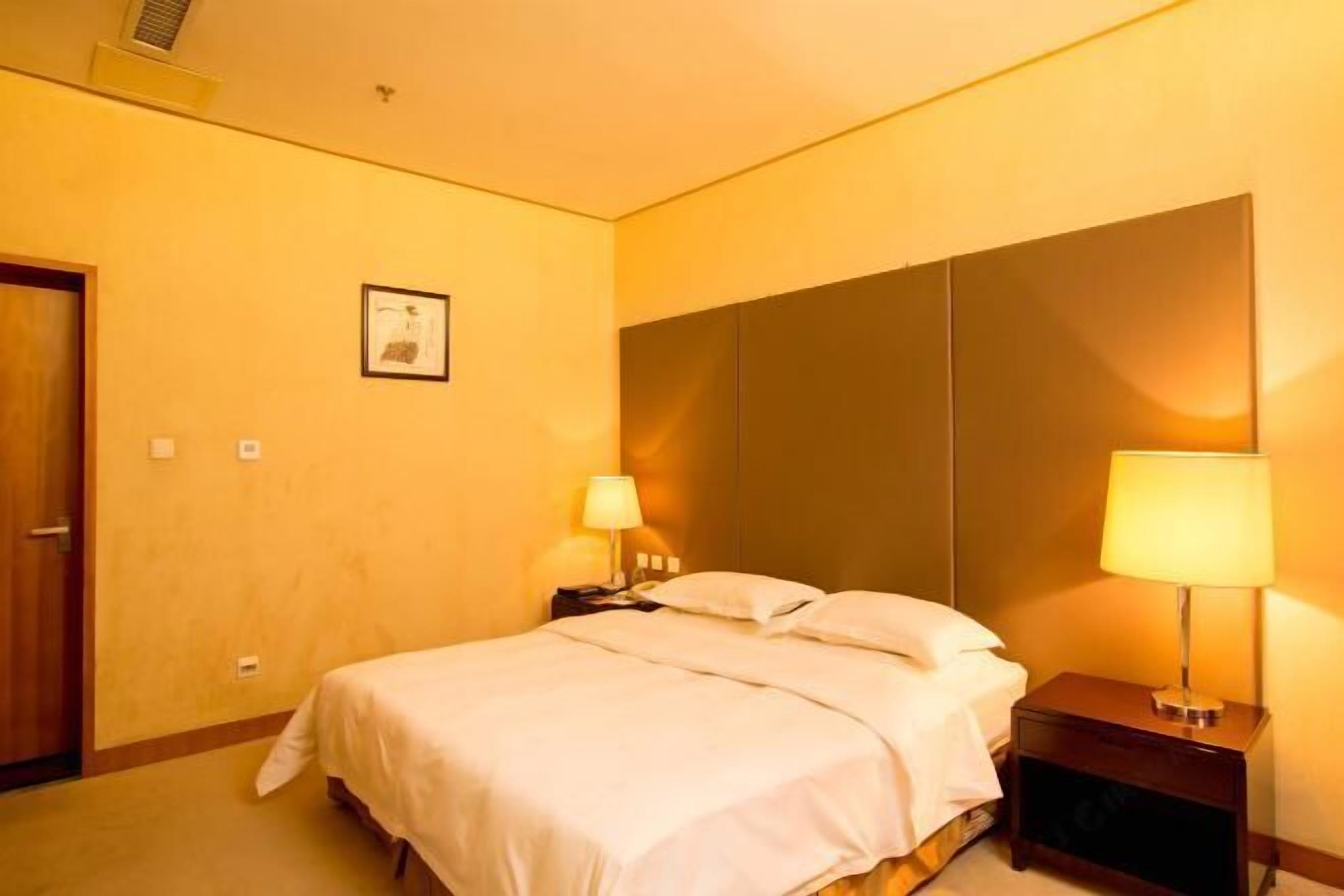 A hotel room with a bed, bedside lamps, a framed picture on the wall, and a door.