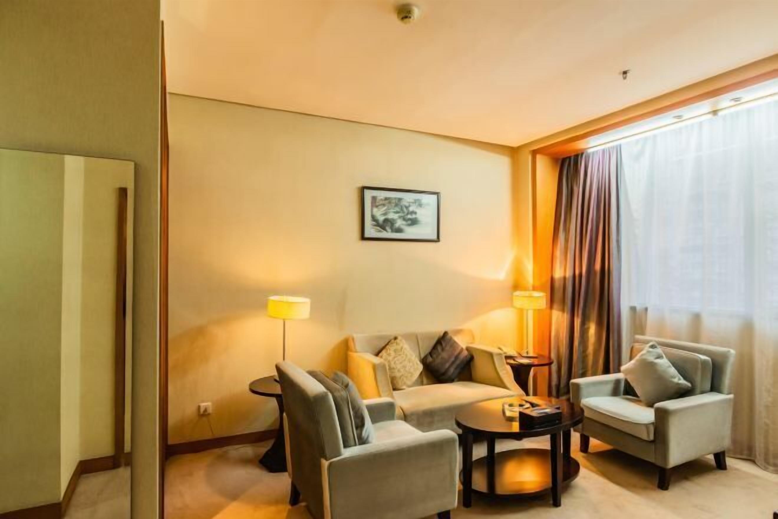 Een hotelkamer met een bank, twee fauteuils, een salontafel, een lamp en een raam met gordijnen.