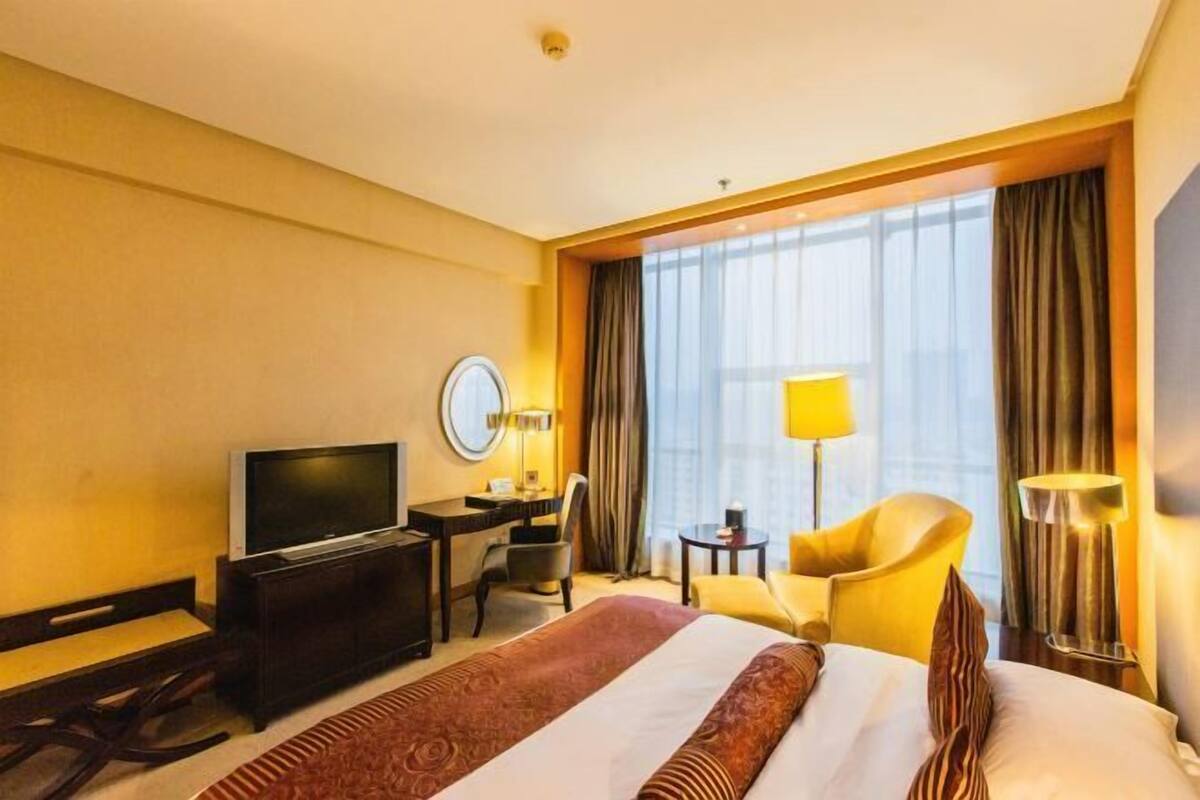 A hotel room with a large bed, a desk with a television, a chair, and a lamp.