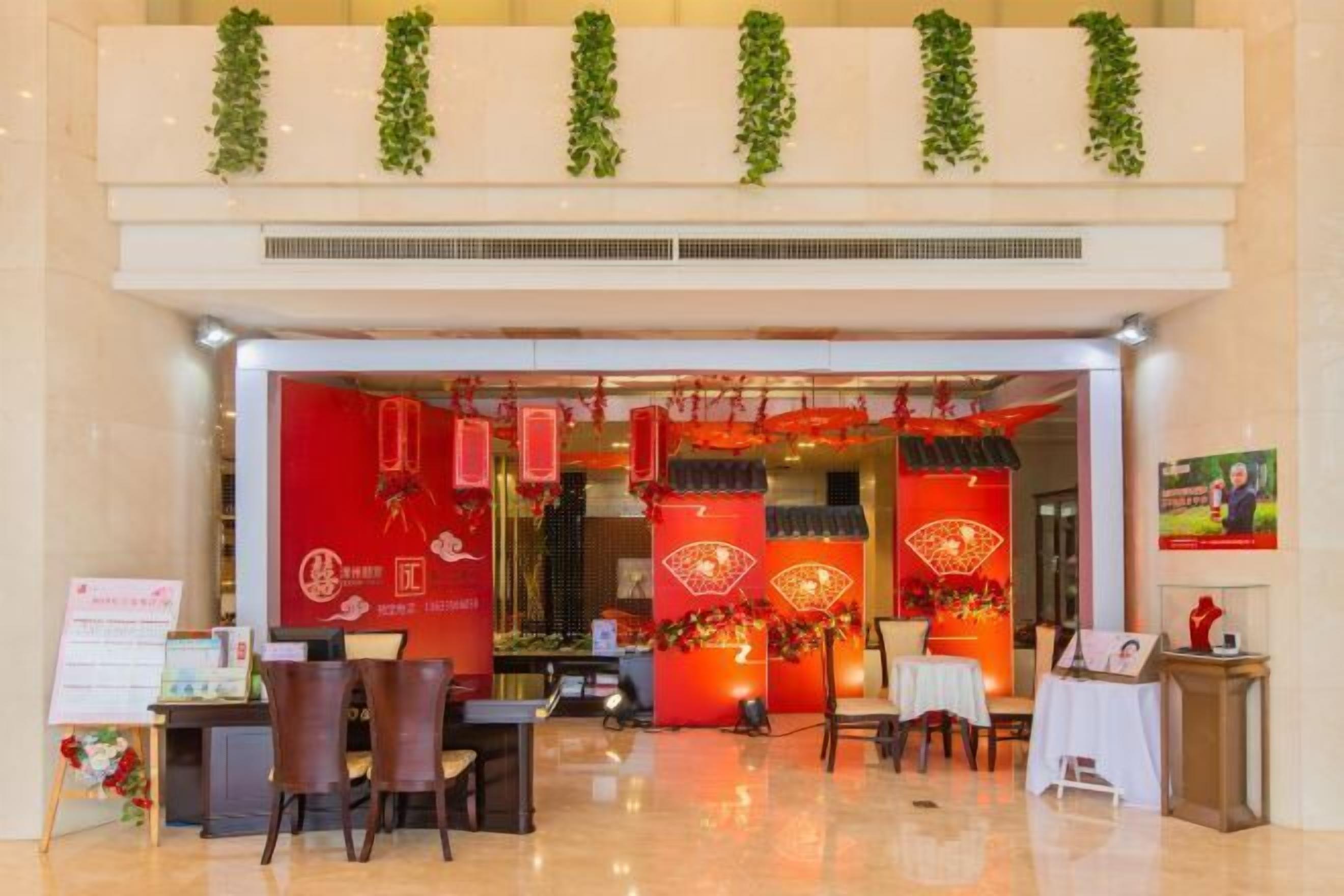 Vestíbulo de hotel con mostrador de recepción, zona de estar y elementos decorativos, incluyendo faroles rojos y plantas verdes.