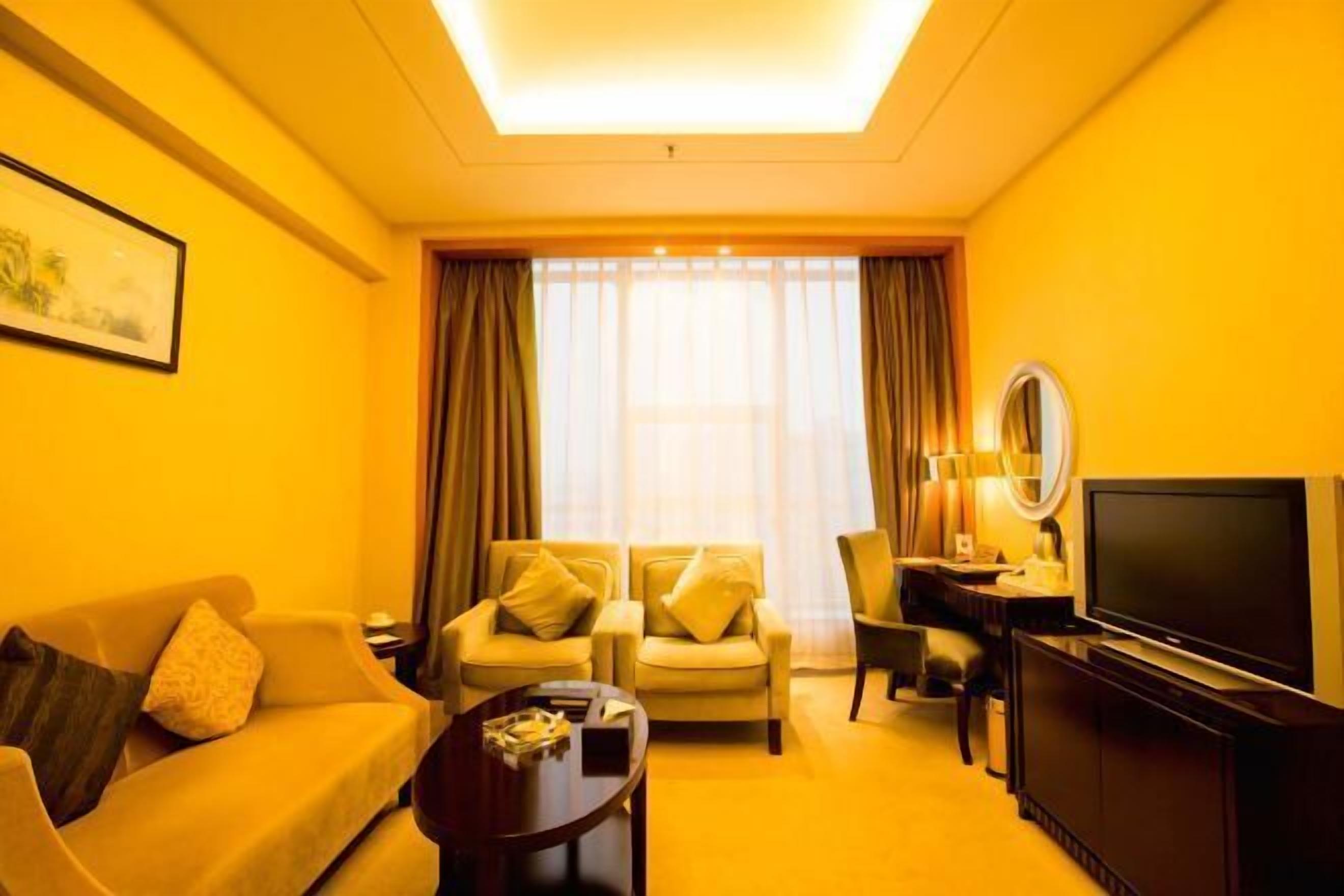 A hotel room with a sofa, two armchairs, a coffee table, a TV, and a large window with curtains.