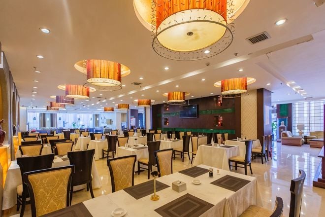Un grand espace dédié à la salle à manger, avec plusieurs tables et chaises, des luminaires au plafond et un écran de télévision fixé au mur.