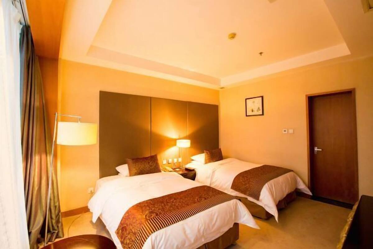 A hotel room with two beds, a nightstand, a lamp, a door, and a wall-mounted picture.