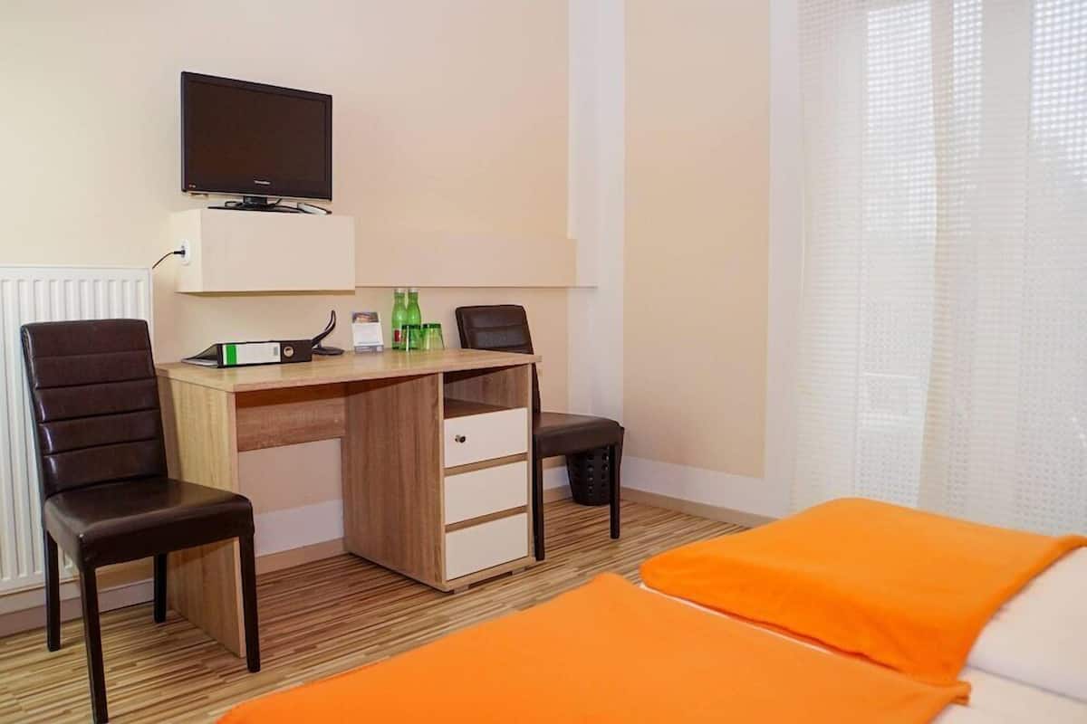 Habitación de hotel con un escritorio de madera, dos sillas, un televisor y una cama con ropa de cama naranja.