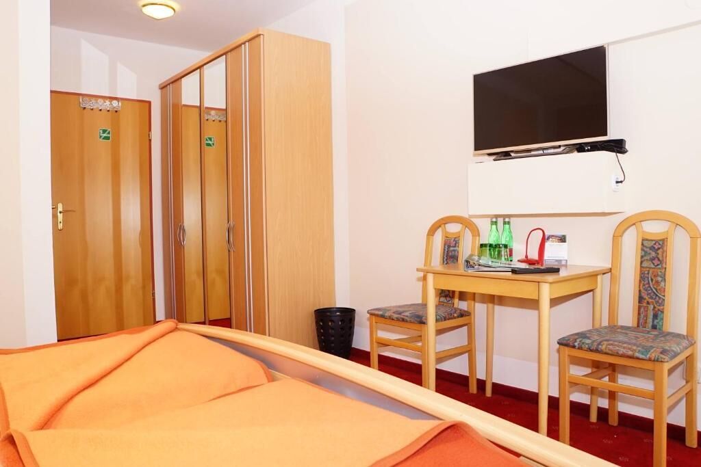 Habitació d'hotel amb un llit, un televisor fixat a la paret, un armari de fusta i una taula petita amb caires.