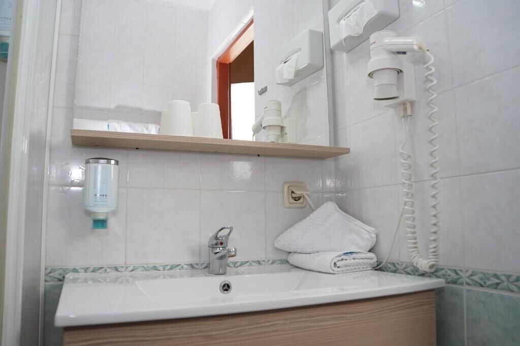Un baño con lavabo, espejo, toallero y un secador de pelo en la pared.
