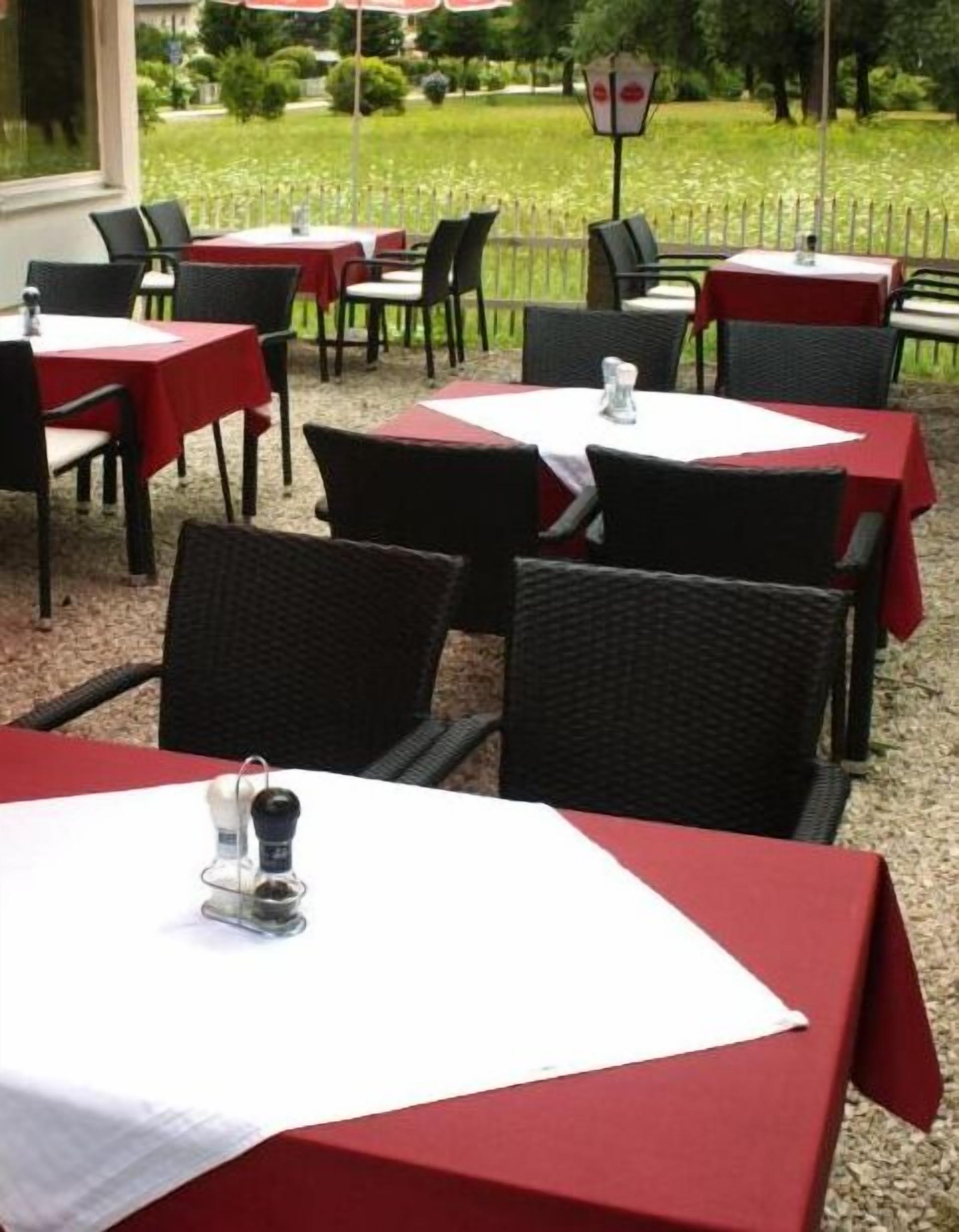 An outdoor dining area with tables covered in red tablecloths and black wicker chairs.