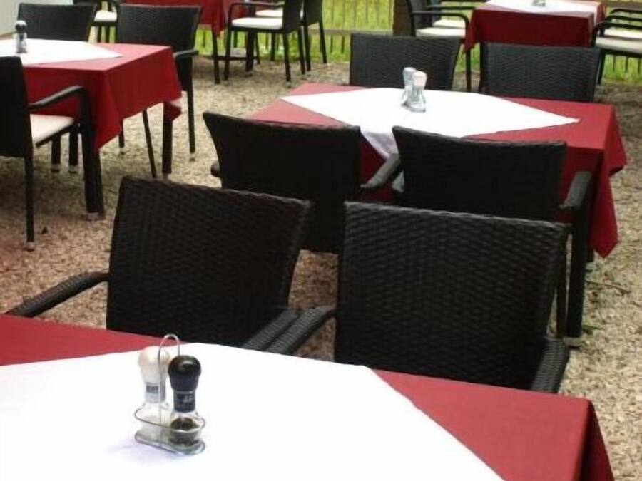 An outdoor dining area with tables covered in red tablecloths and black wicker chairs.