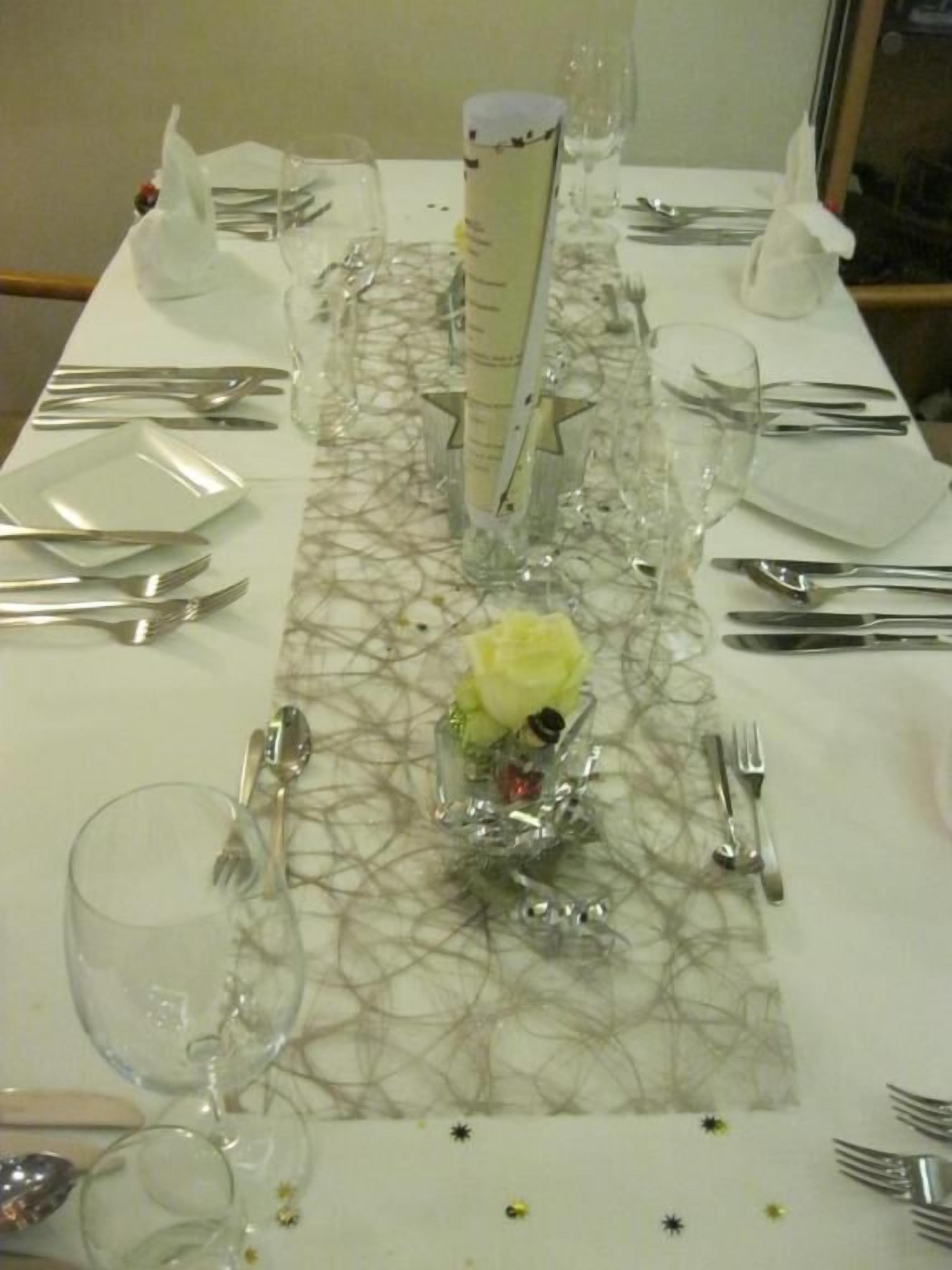 Une table dressée pour un repas, avec de la vaisselle en verre transparent, des couverts et un centre de table.