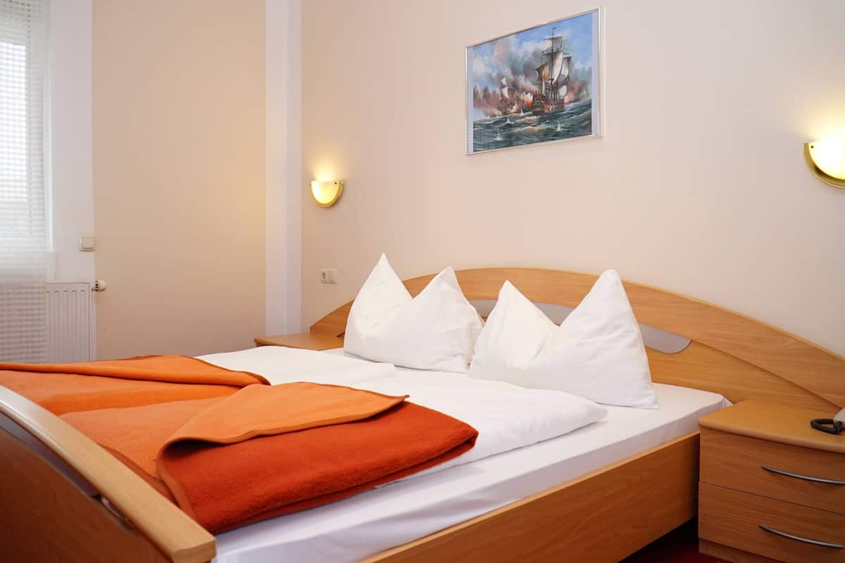 Una cama bien hecha con ropa de cama blanca y naranja, un cabecero de madera y una mesita de noche con cajones.