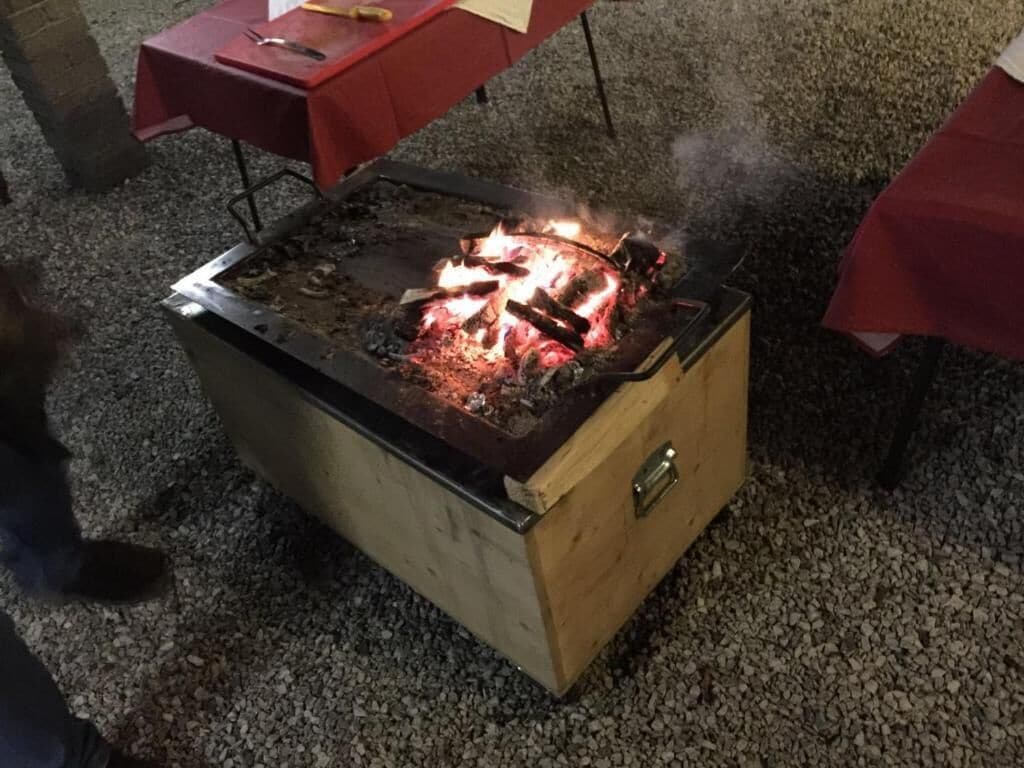 Una barbacoa portàtil amb foc encès a la part superior, sobre un sòl de grava.