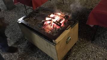 Una barbacoa portàtil amb foc encès a la part superior, sobre un sòl de grava.