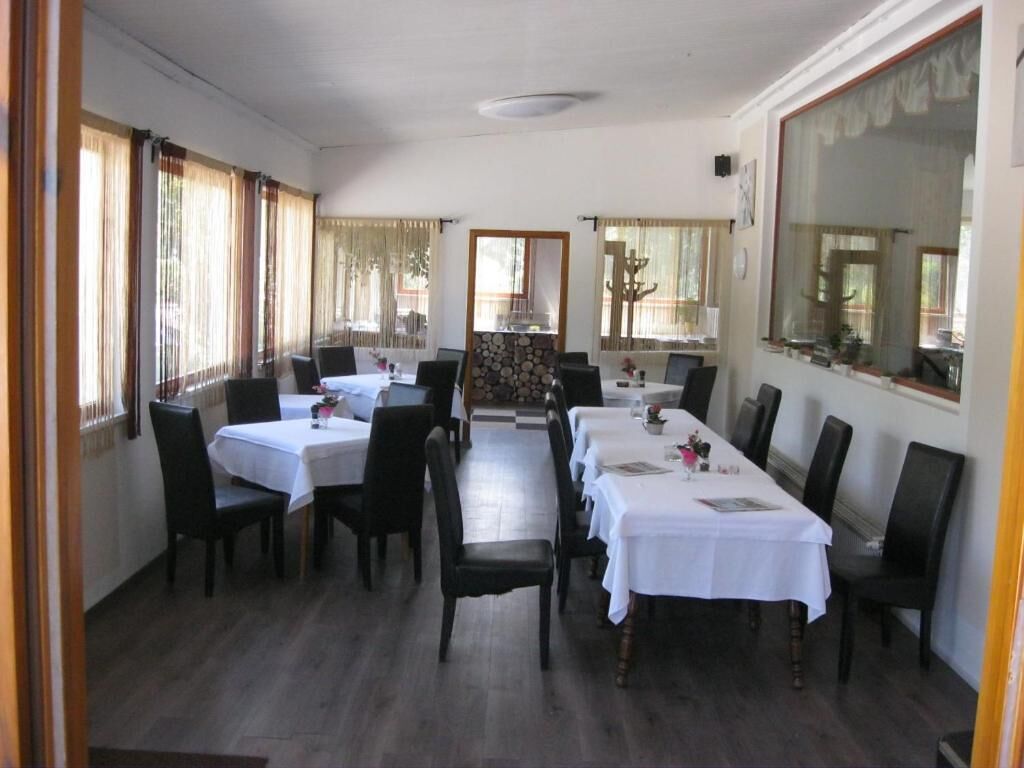 Un comedor con varias mesas y sillas, ventanas amplias con cortinas y vista al exterior.