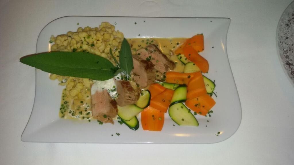 Une assiette blanche contenant un plat composé de viande, de légumes et d’une sauce crémeuse.