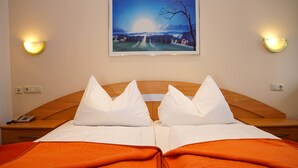 Una habitación de hotel con una cama doble, dos almohadas, un edredón naranja, una mesita de noche con un teléfono y un cuadro en la pared.