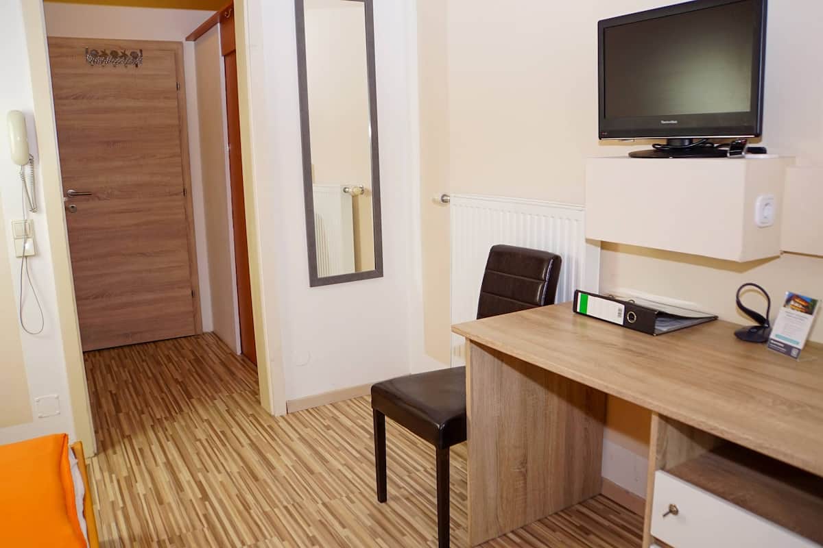 Habitación de hotel con piso de madera, un escritorio con silla, televisor, espejo y teléfono.