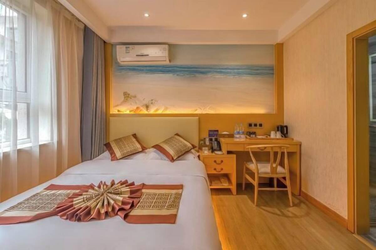 Ein Hotelzimmer mit einem Bett, einem Schreibtisch, einem Sessel und einem Bild mit einer Strandansicht.