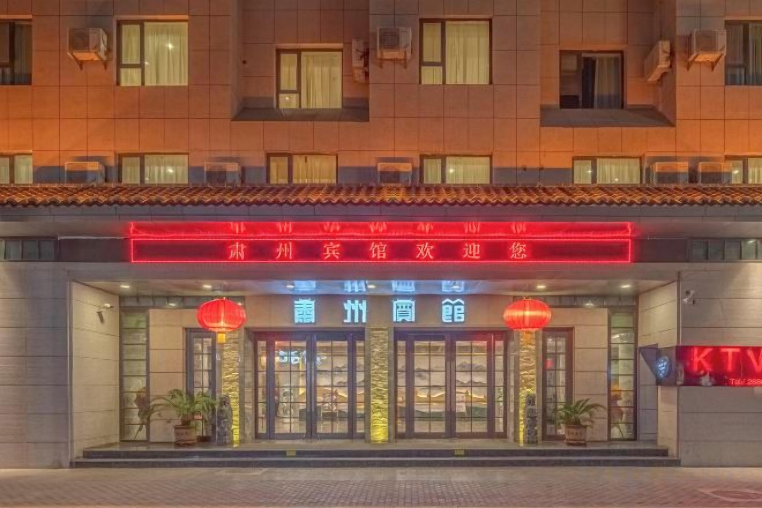 A hotel entrance with a neon sign, glass doors, and potted plants.