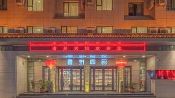 A hotel entrance with a neon sign, glass doors, and potted plants.