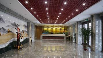 A spacious lobby with a reception desk, a large mural, and a polished marble floor.