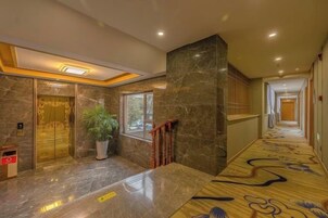 Un vestíbulo de hotel con piso de mármol, una planta en maceta, una escalera y una alfombra estampada.