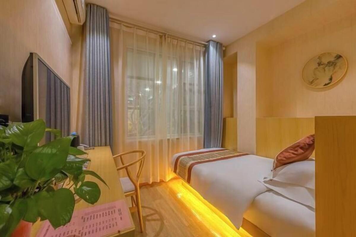 Ein Hotelzimmer mit einem Bett, einem Schreibtisch, einem Sessel, einer Pflanze und einer Wanduhr.