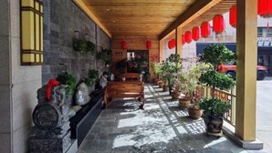 Un espacio al aire libre techado con bancos de madera, plantas en macetas y faroles rojos.