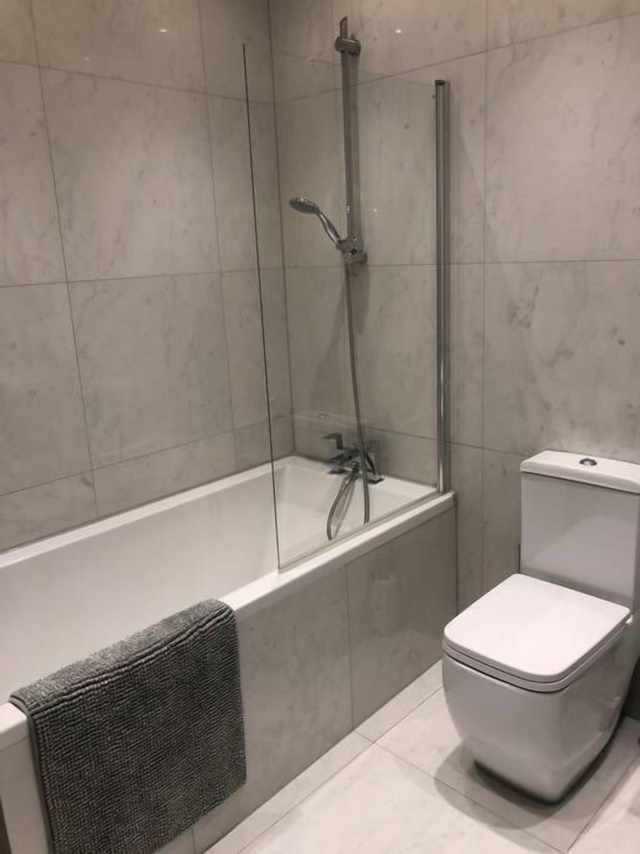Une salle de bain moderne avec une douche à parois de verre, des toilettes blanches et un porte-serviettes.