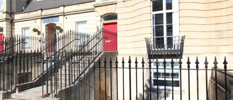 A building with a red door, a black iron fence, and a staircase leading to the entrance.
