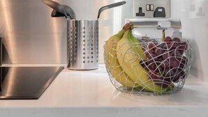 Eine Küchenarbeitsplatte mit Obstkorb, der Bananen und Trauben enthält, einer Metallreibe und einem modernen Herd.