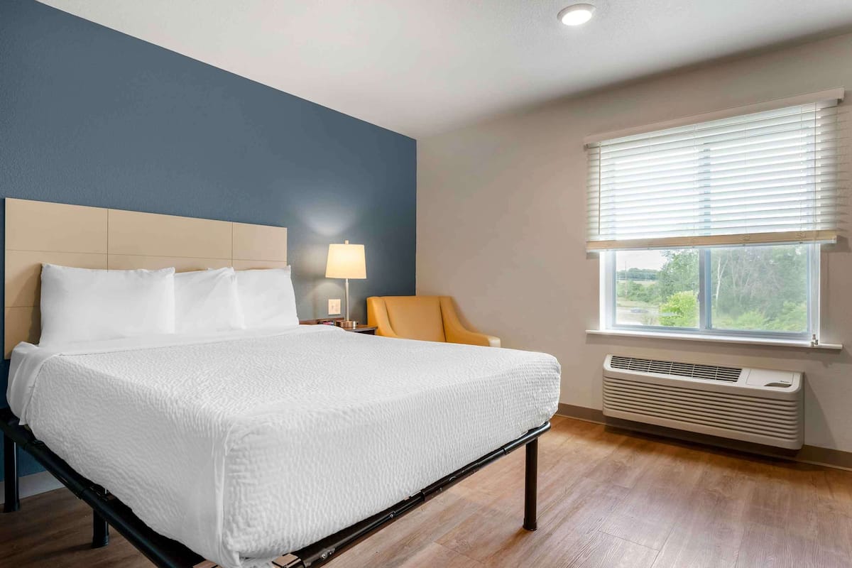 A neatly made bed with white linens, a headboard, and a bedside lamp.