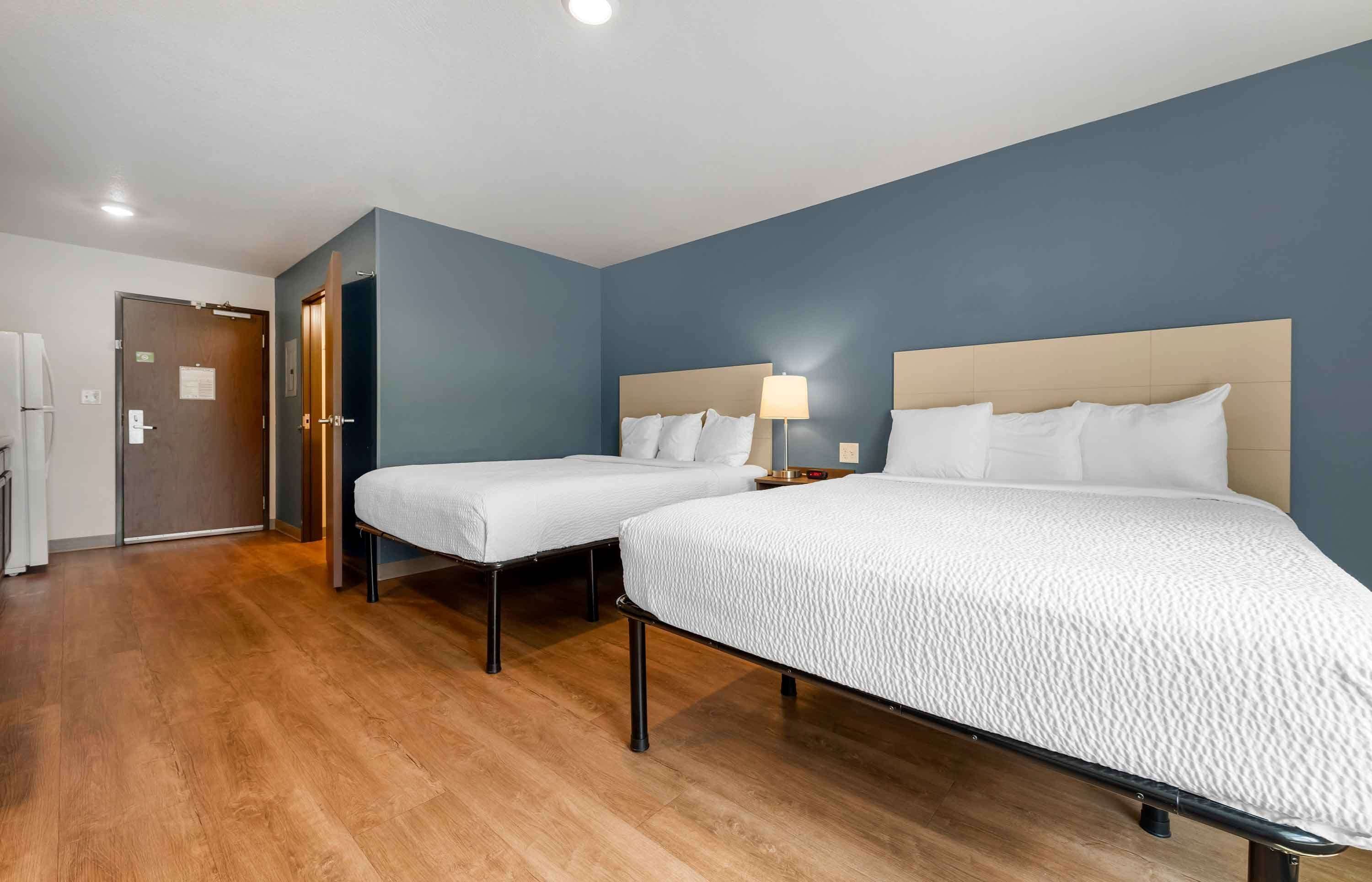 A hotel room with two single beds, a wooden floor, and a blue accent wall.