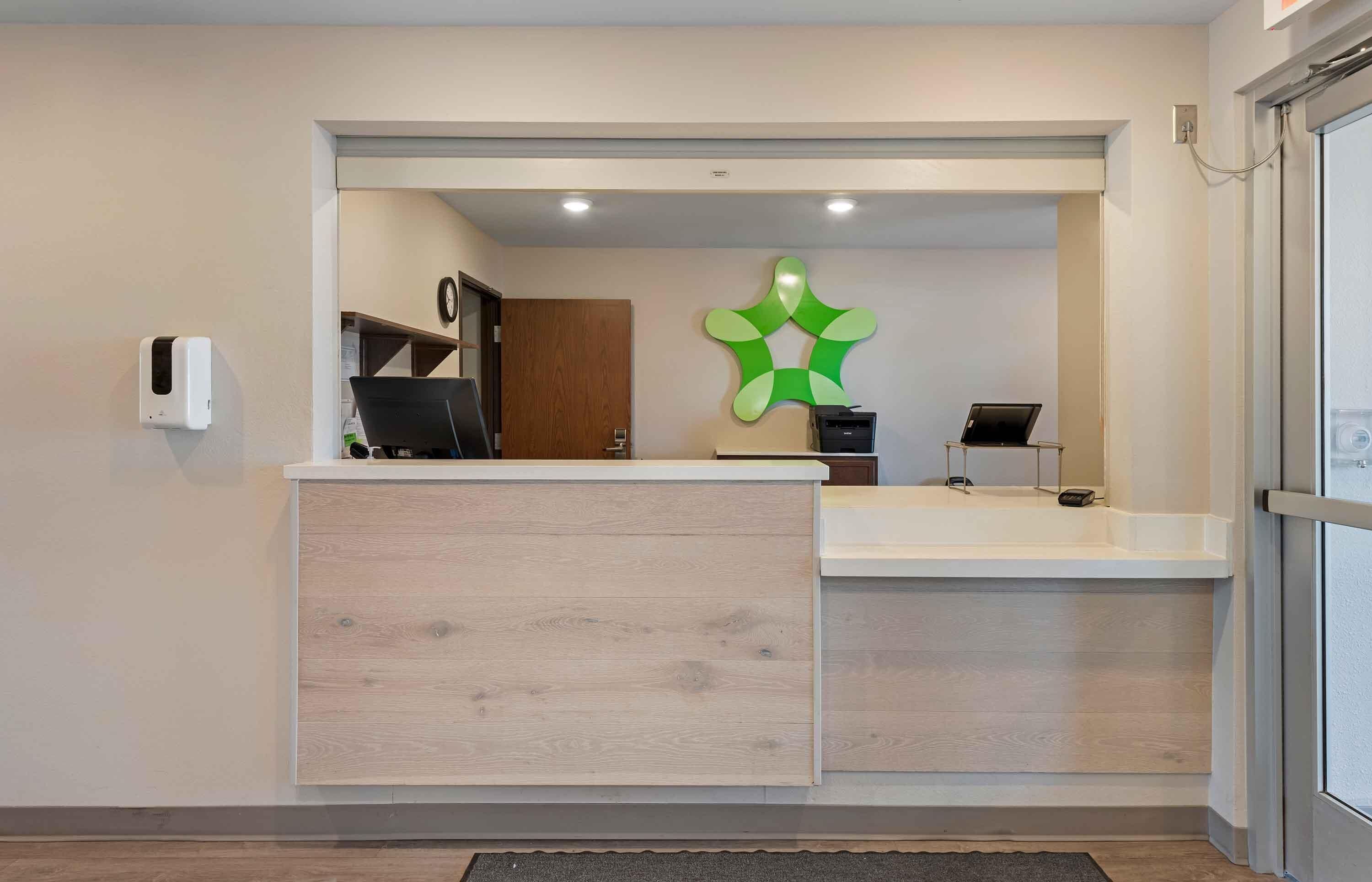 Un área de recepción con un mostrador de madera, un reloj en la pared y un adorno verde en la pared.