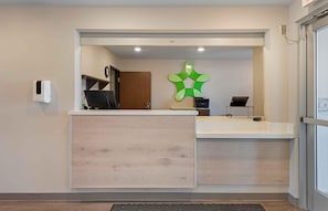 A reception area with a wooden reception desk, a wall-mounted clock, and a green wall decoration. - Extended Stay America Suites - Minneapolis - Airport - Mendota Heights (Mendota Heights)