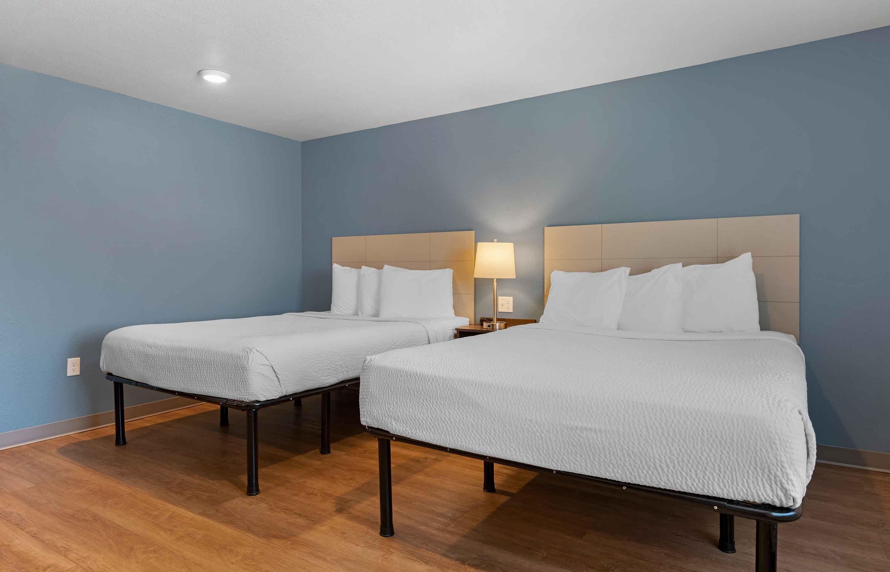 Una habitación de hotel con dos camas individuales, una mesita de noche con lámpara y suelo de madera.