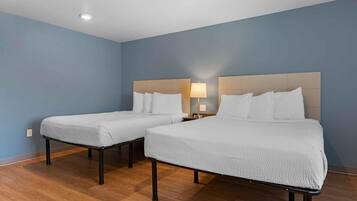 Una habitación de hotel con dos camas individuales, una mesita de noche con lámpara y suelo de madera.