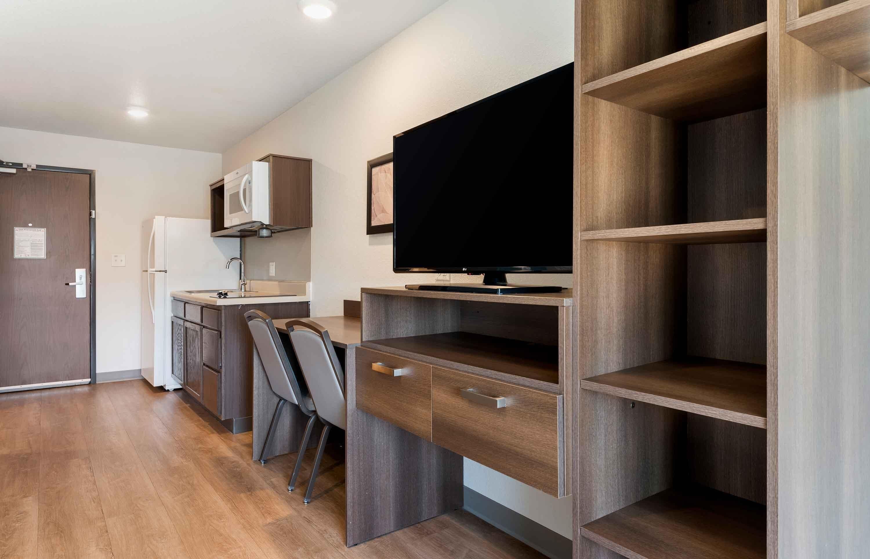 A compact kitchenette with a microwave, sink, and a flat-screen TV mounted on a wooden wall.
