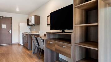 A compact kitchenette with a microwave, sink, and a flat-screen TV mounted on a wooden wall.