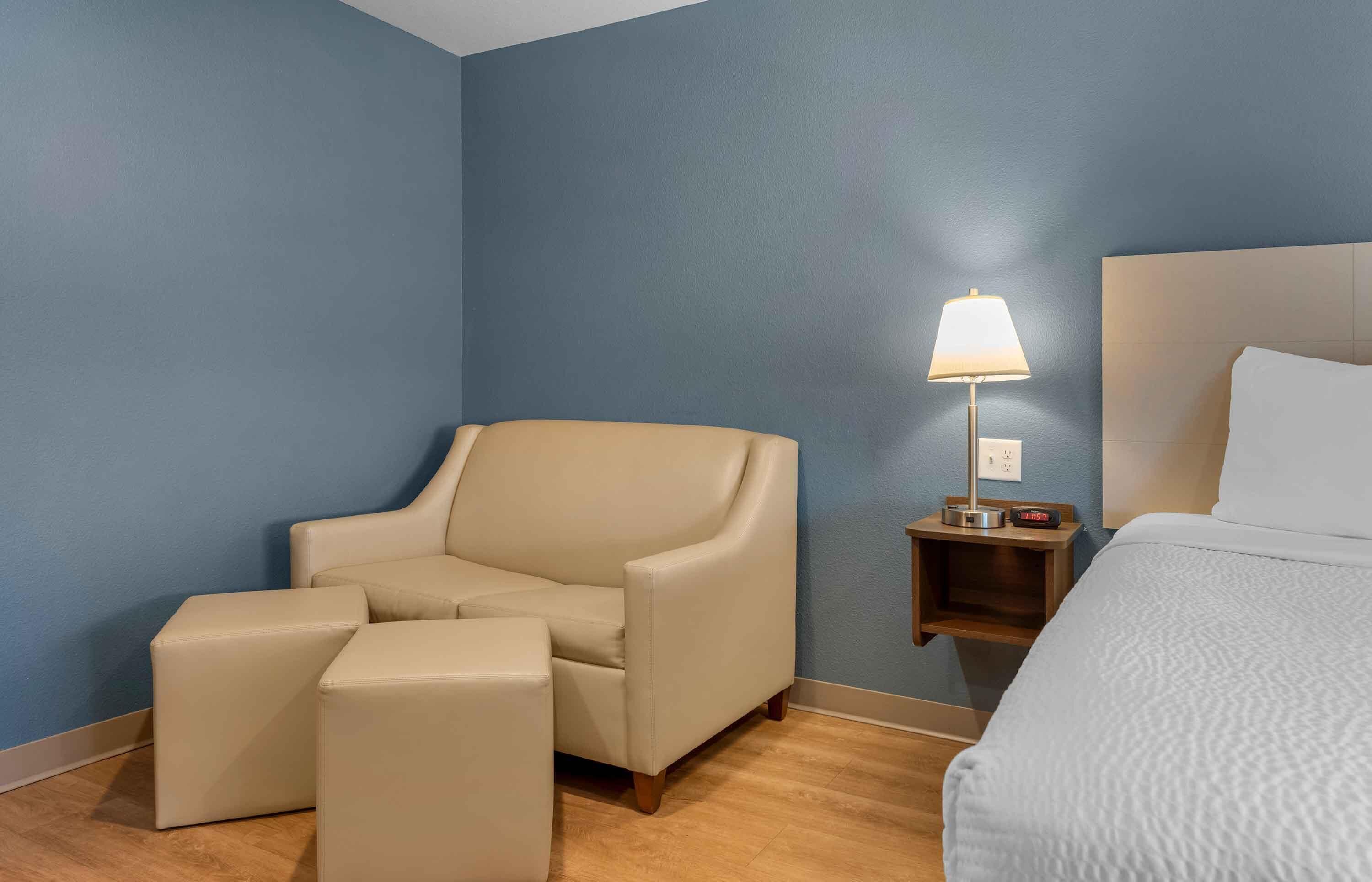 A hotel room with a bed, a chair, a nightstand, and a lamp.