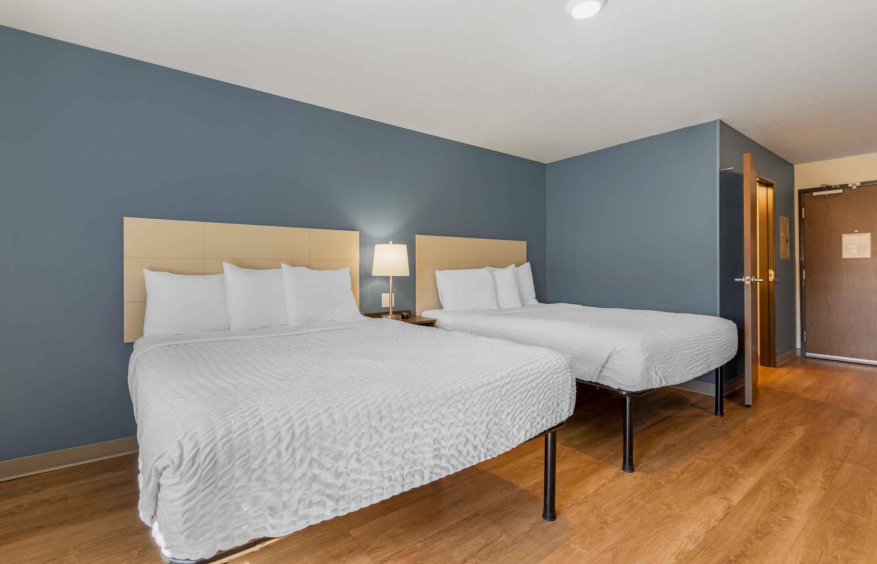 Una habitación de hotel con dos camas, una mesita de noche con lámpara y suelo de madera.